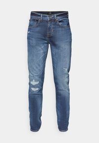 Jeans en denim bleu clair avec une coupe slim, dotés de patches déchirés, d'une texture délavée et d'une taille standard avec fermeture à bouton.