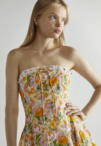 Vestido sin mangas con estampado floral, que presenta un borde de encaje, patrones de flores coloridos en naranja y rosa, con un cuerpo ajustado y detalles de botones.