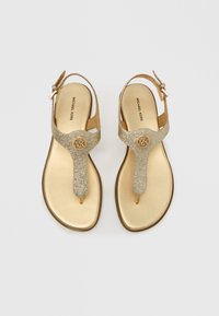Σανδάλια χρυσής γκλίτερ με λουράκι σε σχήμα κύκλου με λογότυπο, ρυθμιζόμενο λουράκι αστραγάλου και λείο μεταλλικό πέλμα. Σχέδιο με επίπεδη σόλα.