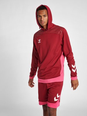 Czerwona sportowa bluza z kapturem z fakturowanym wzorem na ramionach, w komplecie z czerwonymi szortami z różowymi akcentami i białymi detalami logo.