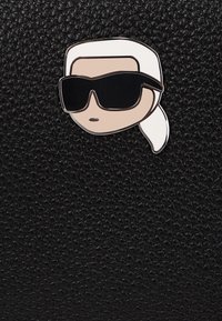 Black textured background with a shiny pin featuring a cartoon face with sunglasses, light hair tied back, and minimal detailing.