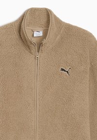 Chaqueta de forro polar beige con cuello alto y cremallera completa. Presenta una superficie suave y texturizada y un logo negro de Puma en el lado izquierdo del pecho.