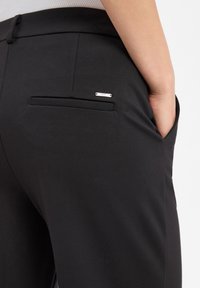 Black trousers featuring a sleek design and textured fabric. Notable details include a rear pocket with a silver accent and clean stitching.