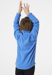 Modrý fleecový pulovr s dlouhými rukávy, vysokým límcem a texturovanou tkaninou. Zadní pohled ukazuje uvolněný střih a zakulacený lem.