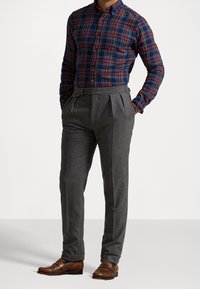 Koszula w kratę w kolorach granatowym i bordowym, zestawiona z szarymi spodniami plisowanymi. Brązowe buty z dekoracyjnymi akcentami.