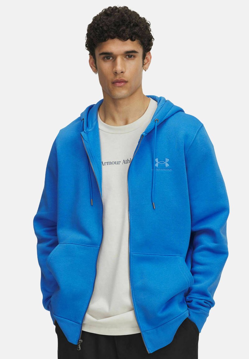 Sudadera azul con cremallera, capucha ajustable y bolsillos frontales, hecha de una tela suave. Lleva encima una camiseta blanca con texto impreso.