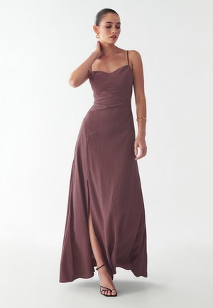 Dlhé, hnedé maxi šaty vyrobené z textúrovanej tkaniny, s tenkými ramienkami a rozparkom až po stehno, doplnené čiernymi sandálmi na remienky.