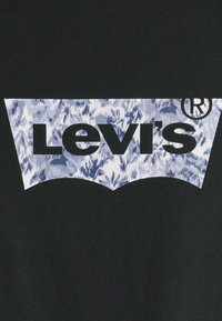 Levi's logotyp med svart text på en blå och vit marmorerad bakgrund, placerad på en svart tygyta.