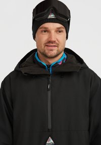 Zwarte buitenjas met rits aan de voorkant, capuchon en O'Neill-logo. Binnenste kraag met een blauw en roze patroon zichtbaar. Zwarte gebreide beanie en skibril gedragen.