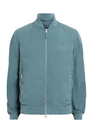 Vaaleansininen pommikurta, valmistettu sileästä kankaasta; siinä on vetoketju edessä, ribbilikudot ja sivutaskut hopeisilla yksityiskohdilla.