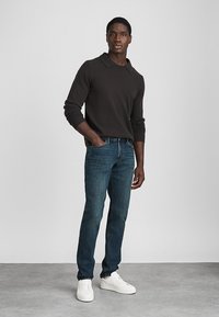 Sötétbarna kötött pulóver gallérral, sötétkék farmernadrággal párosítva. Az öltözéket fehér sportcipők egészítik ki.