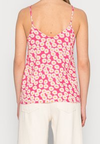 Top de tirantes florales con fondo rosa, que presenta margaritas blancas con centros amarillos, tirantes finos y un diseño en la espalda en forma de V.