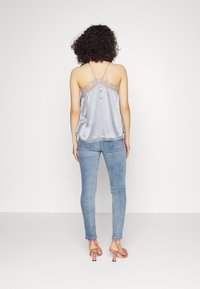 Zijdegrijze cami met kantaccenten, dunne verstelbare bandjes, gecombineerd met licht denim jeans en roze hakken, getoond vanuit de achterkant.