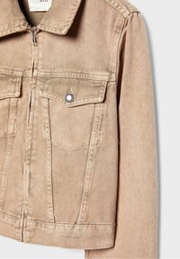 Veste en denim beige avec fermeture éclair devant, col pointu, poches à rabat avec détails boutonnés, et coutures visibles sur un fond uni.