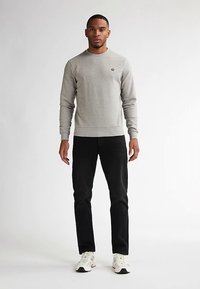 Ανοιχτό γκρι φούτερ, με στρογγυλή λαιμόκοψη, ριμπ μανσέτες και τελείωμα. Φορεμένο με μαύρο τζιν και λευκά αθλητικά παπούτσια. Απλός σχεδιασμός με λεπτομέρεια λογότυπου.