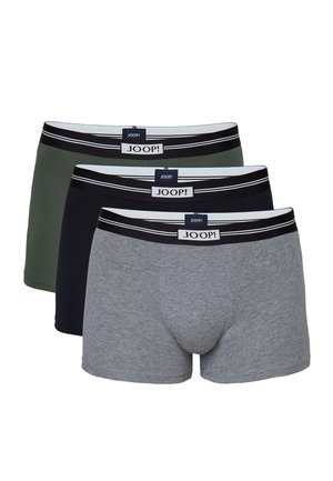 Muskelbepackter Mann steht barfuß nach vorne gerichtet, trägt schwarze enganliegende Boxershorts mit Joop!-Label am Bund.