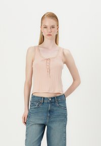 Light peach, ribbed cropped tank top with a square neckline, decorative buttons down the front, and scalloped accents along the straps.