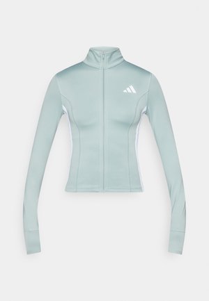 Veste de sport vert clair avec un col haut, une fermeture éclair complète à l'avant, des panneaux latéraux blancs et un petit logo blanc en haut à gauche.