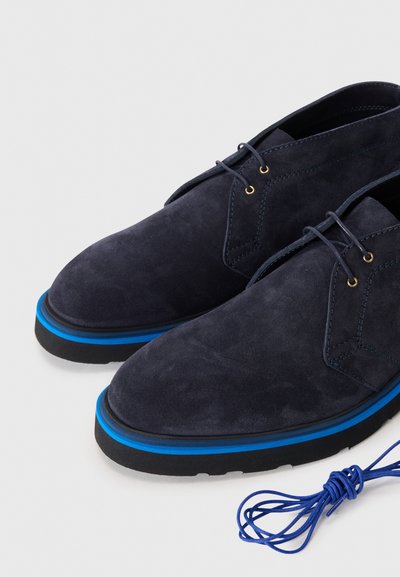 Chaussures en suède bleu marine avec des accents bleus, présentant une pointe arrondie et une surface texturée. Comprend des lacets bleus assortis.