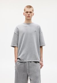 Sivý oversized tričko s krátkymi rukávmi, okrúhlym výstrihom, vyrobené z mäkkej bavlny, s nenápadným logom na ľavej strane hrude.