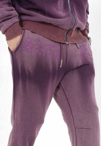 Lila Sweatshirt und Jogginghose aus einem strukturierten Stoff. Die Jogginghose hat "SIXTH" in Lila auf dem linken Taschenbereich aufgedruckt.
