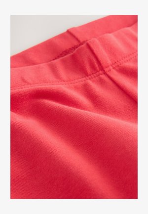 Korálová látka s hladkou textúrou a elastickým pásom, vybavená jemnými švovými detailmi. Materiál vyzerá mäkko a pružne.