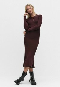 Burgundy ribbed knit dress with a fitted silhouette, collared neckline, and front button details. Paired with black ankle boots.