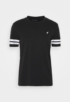 T-shirt noir à manches courtes en coton, avec des rayures blanches sur chaque manche et un petit logo d'oiseau sur la poitrine.