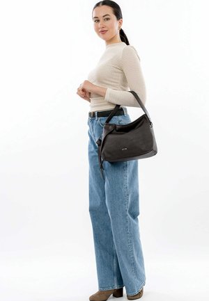 Sac en cuir noir avec une texture lisse, au design décontracté, à courte anse, et avec un logo distinctif. Porté avec un jean large bleu clair et un haut crème.