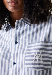 Blue and white striped button-up shirt with a chest pocket featuring an embroidered logo, crafted from lightweight fabric.