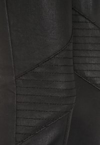 Primer plano de una tela negra con líneas de costura en diagonal que crean un patrón geométrico y texturizado en la superficie de una prenda.