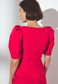 Blusa fucsia a maniche corte con spalle a sbuffo e scollatura quadrata. Tessuto morbido, vestibilità aderente e cuciture minime. Vista posteriore mostrata.
