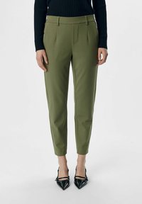 Olivengröna skräddarsydda byxor med platt front, smala ben och sidofickor, matchade med svarta lackpumps med spetsig tå.