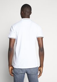 Hvid kortærmet polo-shirt med sorte kanter ved kraven og ærmerne, designet med en klassisk pasform, bagview viser minimalt detaljering.