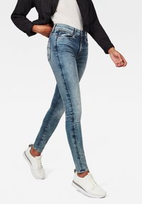 Smaljeans i blekt blå denim med hög midja, fem fickor och en slank silhuett, tillsammans med vita sportiga snörskor.