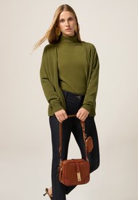 Khaki zielony sweter z dzianiny nałożony na dopasowany golf, zestawiony z ciemnoniebieskimi dżinsami. Mała brązowa torebka na złotych akcentach i pasku.