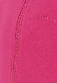 Różowa kurtka na zamek wykonana z gładkiej mieszanki bawełny, z wyraźnym suwakiem i wytłoczonym logo na wysokości klatki piersiowej.