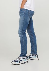 Jeans de denim azul ajustados con un acabado desgastado, cinco bolsillos y detalles de costura. Combinados con zapatillas deportivas blancas y marino.