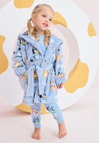 Accappatoio in pile blu con stampe di personaggi e tasche frontali, abbinato a leggings blu con illustrazioni colorate di animali. Texture morbida.