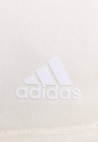Bílá atletická látka s vyvýšeným bílým logem Adidas se třemi pruhy, hladkou texturou a viditelným prošíváním.