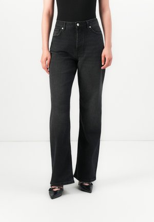 Person wearing high-waisted black wide-leg jeans with front pockets and black pointed-toe heels against a white background.