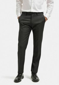 Grå skräddarsydda byxor gjorda av ett texturerat, lättviktigt tyg. Har en smal passform, veckad front och sidfickor. Bärs med svarta skor.