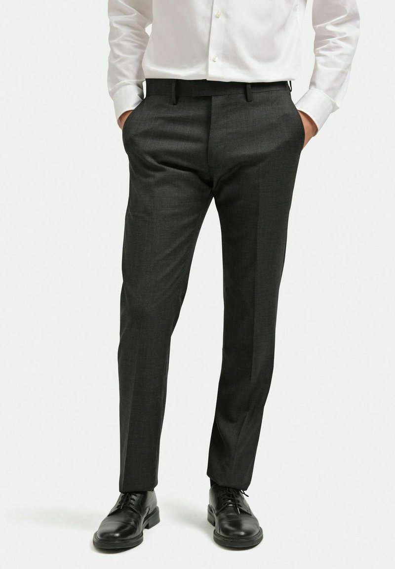 Grå skräddarsydda byxor gjorda av ett texturerat, lättviktigt tyg. Har en smal passform, veckad front och sidfickor. Bärs med svarta skor.