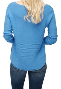 Pull bleu à manches longues côtelé avec une coupe décontractée et un col arrondi, associé à un jean bleu foncé. Tissu texturé avec une finition douce.