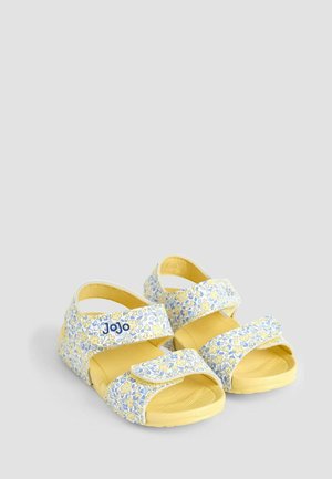 Žlté sandále s kvetinovým vzorom a modrými akcentmi, s nastaviteľnými popruhmi a štruktúrovanou podrážkou pre lepšiu priľnavosť. Názov značky "JoJo" je viditeľný.