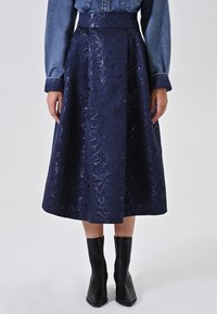Een marineblauwe midi-rok met bloemenborduursel, een gladde textuur en een gestructureerde tailleband, gecombineerd met zwarte enkellaarsjes.
