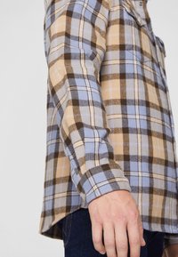 Camicia di flanella con motivo a quadri nei colori beige, marrone e azzurro chiaro. Texture morbida, design con bottoni e dettagli visibili ai polsini.