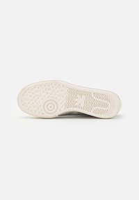 White sneaker sole with circular and wavy traction patterns, Adidas logo near the heel on a plain white background.