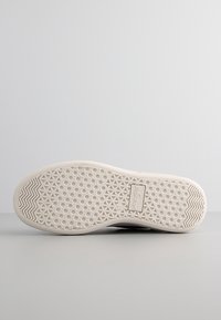 Gummisulor med mönstrad greppfunktion, ljusbeige färg, platt design och logotags. Släta kanter och inga synliga tecken på slitage.