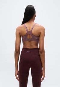 Γυναι κείο αθλητικό σουτιέν σε απαλό μωβ χρώμα με ρυθμιζόμενες τιράντες, σχεδιασμό με άνοιγμα στο πίσω μέρος και κούμπωμα με άγκιστρο. Συνδυάζεται με σκούρο βυσσινί κολάν.